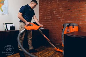 water damage restoration technician vacuums water in office
